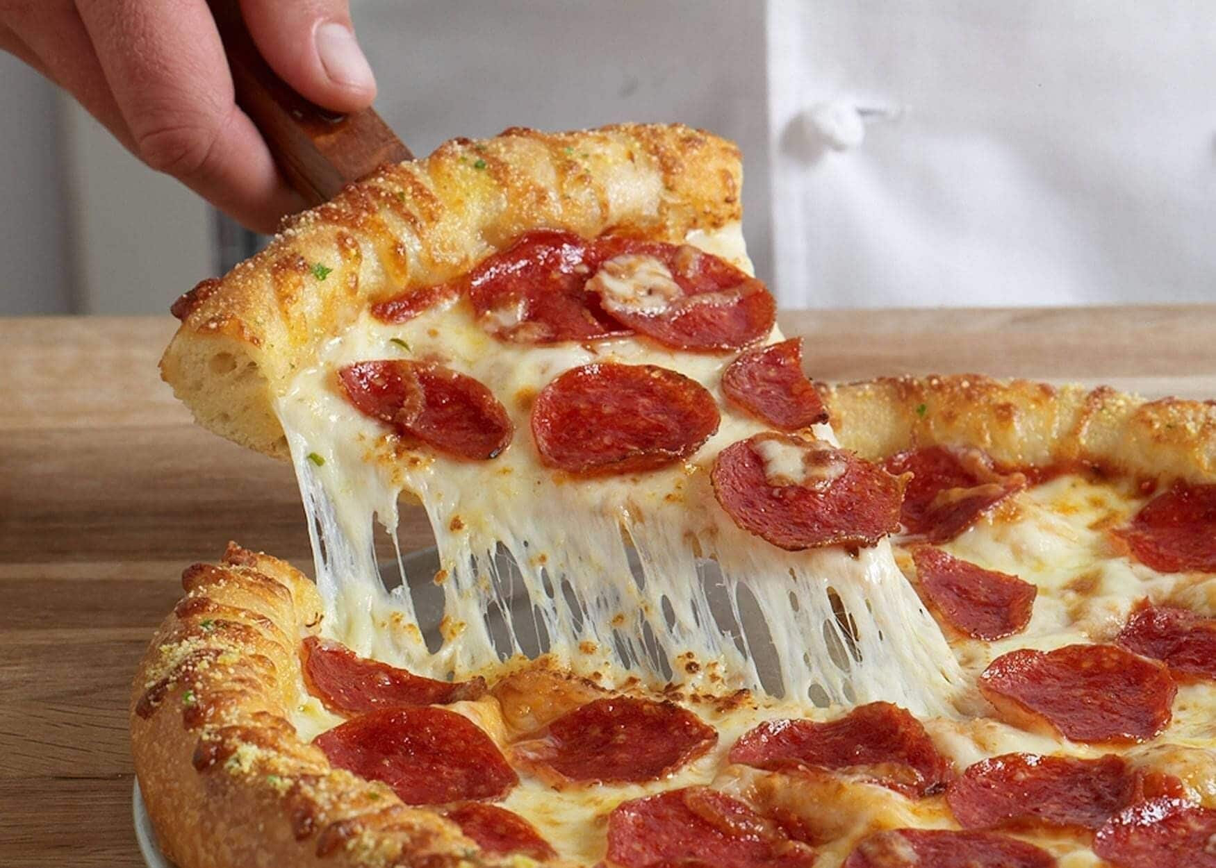 Una mano levanta una pizza con rodajas de pepperoni y queso fundido.