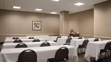 A conference room with multiple tables and chairs, a framed picture on the wall, and a coffee station.