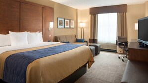 Une chambre d’hôtel avec un grand lit, un bureau, une chaise, une télévision et une fenêtre avec des rideaux.