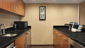 Una cocina moderna con armarios de madera, un lavamanos de acero inoxidable, una cafetera y un cuadro en la pared.
