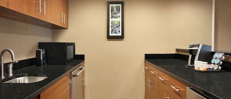 A modern kitchen with wooden cabinets, a stainless steel sink, a coffee machine, and a framed picture on the wall.