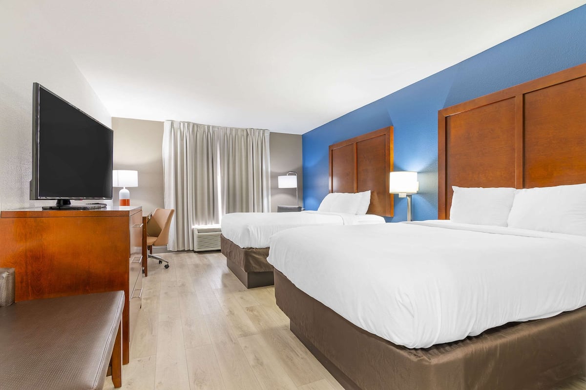 A hotel room with two beds, a desk with a TV, a chair, and a lamp.