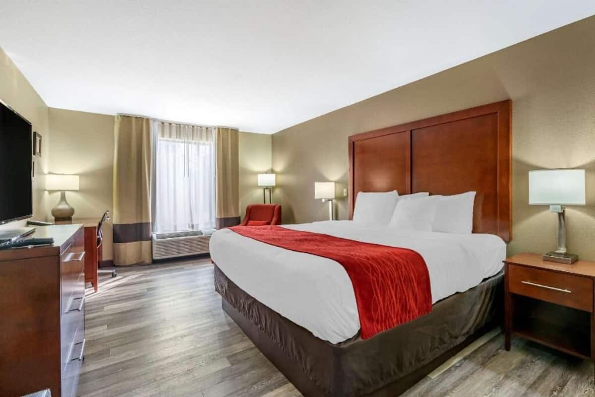 A hotel room with a large bed, a desk, a chair, a TV, and a window with curtains.