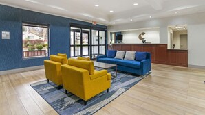 A spacious living area with a blue wall, yellow armchairs, a blue sofa, and a wooden coffee table. - Comfort Inn Near Six Flags St. Louis (Pacific)
