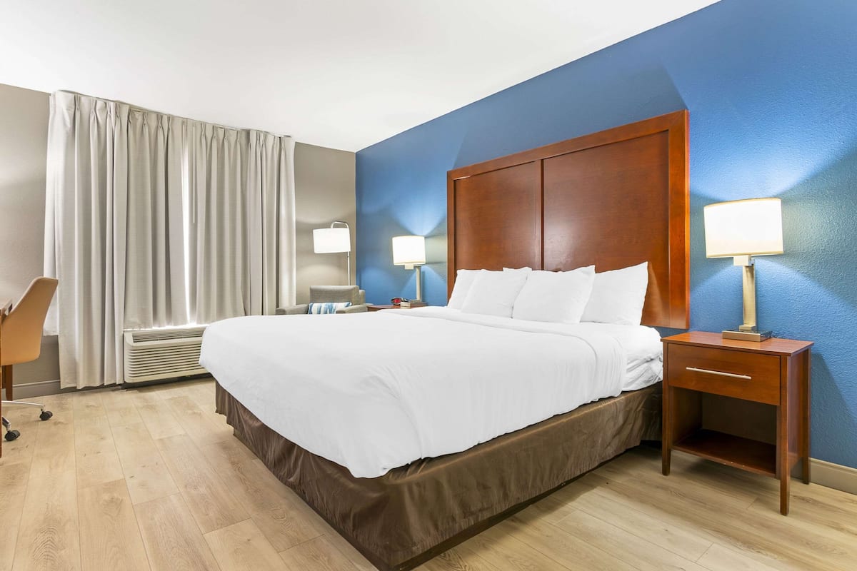 A hotel room with a large bed, two bedside tables with lamps, a desk, and a chair.
