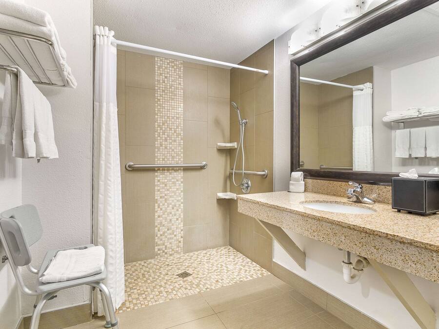 Un baño con ducha, lavamanos, una silla y un espejo.