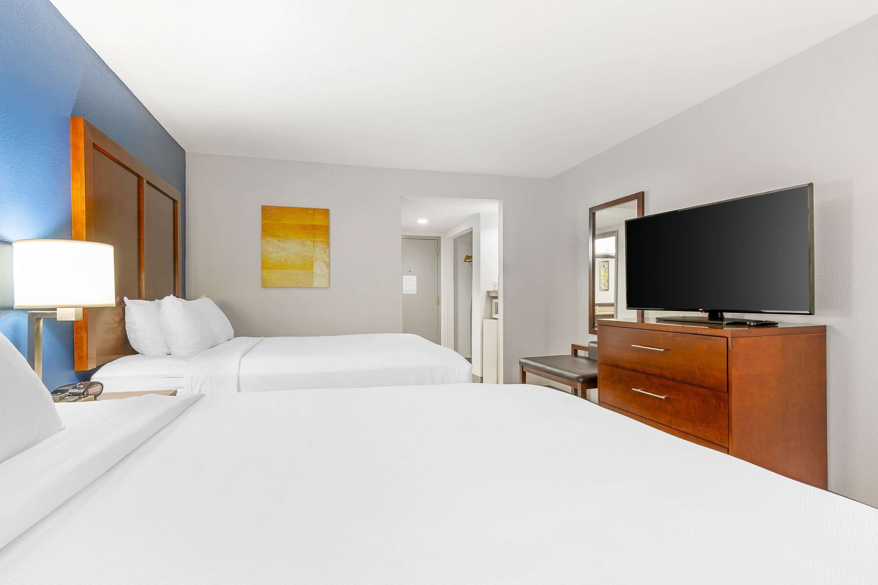 Una habitación de hotel con dos camas, un televisor, un aparador de madera y un cuadro en la pared.