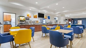 A modern dining area with yellow and blue chairs, a flat-screen TV, and a kitchen area with appliances. - Comfort Inn Near Six Flags St. Louis (Pacific)