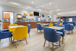 Un comedor moderno con sillas amarillas y azules, un televisor de pantalla plana y una cocina con electrodomésticos.