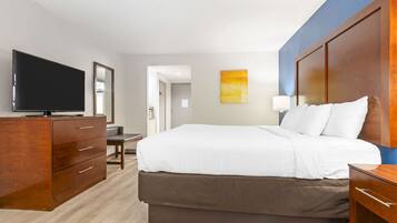 A hotel room with a large bed, wooden dresser, flat-screen TV, and a painting on the wall.