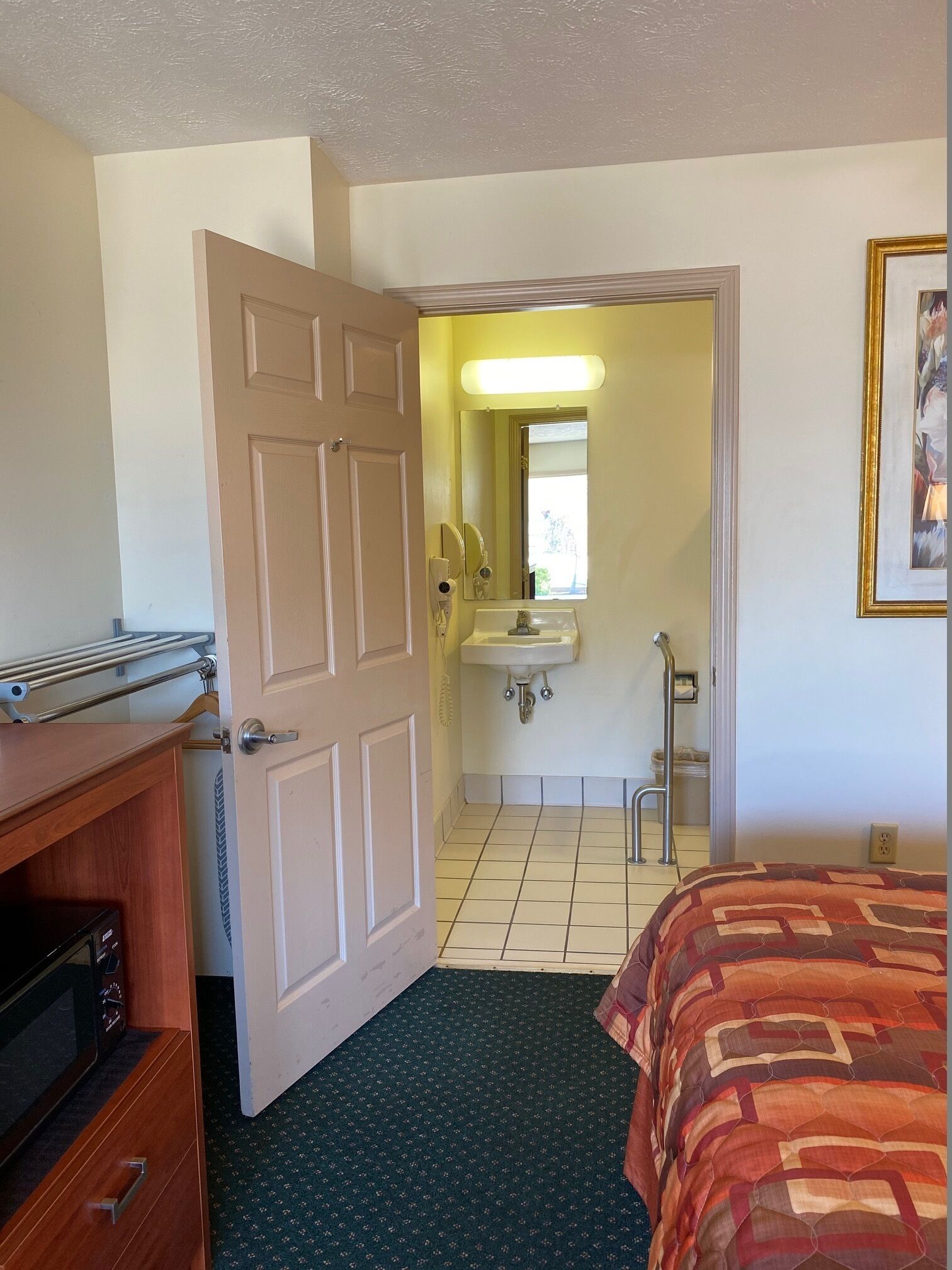 A hotel room with a bed, a dresser, a bathroom with a sink and mirror, and a door leading to another room.
