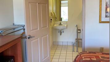 A hotel room with a bed, a dresser, a bathroom with a sink and mirror, and a door leading to another room.