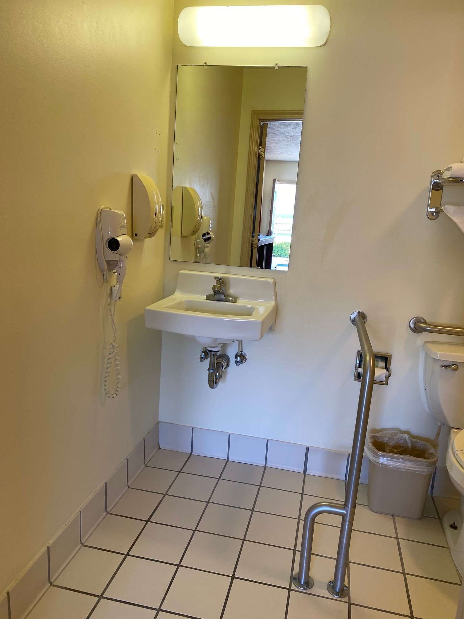 Ein Badezimmer mit Waschbecken, Spiegel, Handtrockner und Mülleimer.