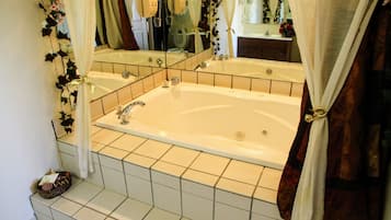 A bathroom with a large bathtub, a mirror, and a shower area.