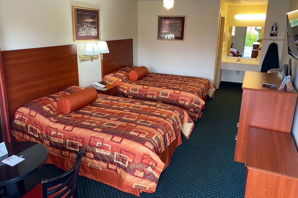 Une chambre d’hôtel avec deux lits, un bureau, une chaise, une lampe de bureau, un téléphone et un miroir.