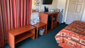 Habitación de hotel con escritorio de madera, televisor, cama con cubrecama estampado y ventilador de techo. Señal de 'No Fumar'.