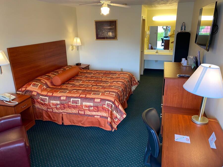 Habitación de hotel con una cama grande, un escritorio, una silla, una lámpara de escritorio, un teléfono, un espejo y un ventilador de techo.