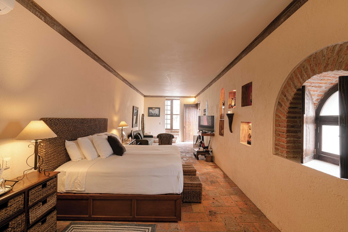 Ein Hotelzimmer mit einem großen Bett, einem Fernseher, einem Schreibtisch mit Lampe sowie einem Kamin aus Ziegelsteinen.