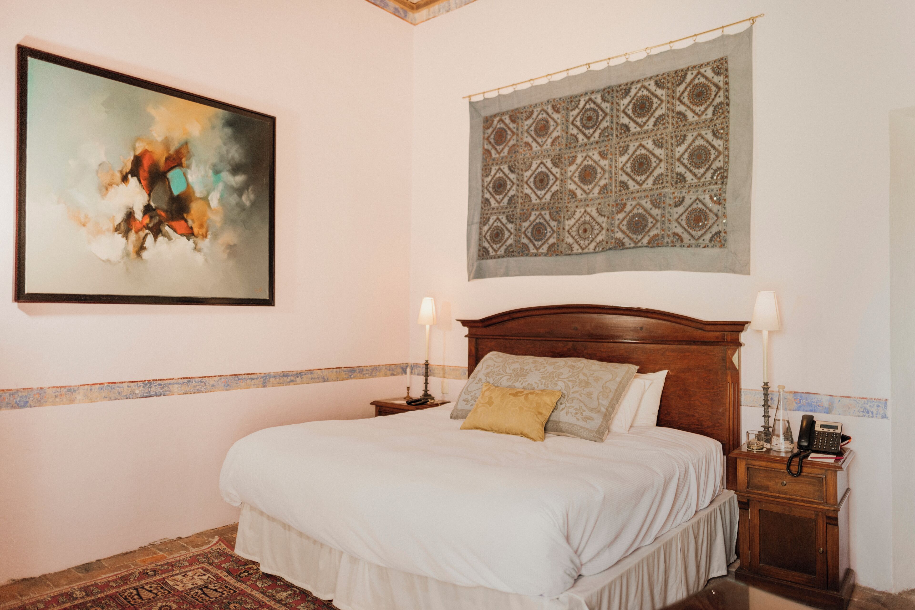 A bedroom with a bed, two bedside tables, a wall tapestry, and a painting.