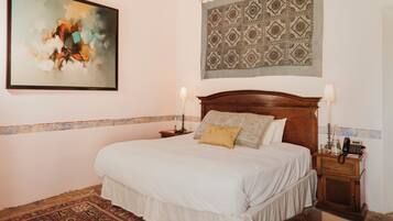 A bedroom with a bed, two bedside tables, a wall tapestry, and a painting.