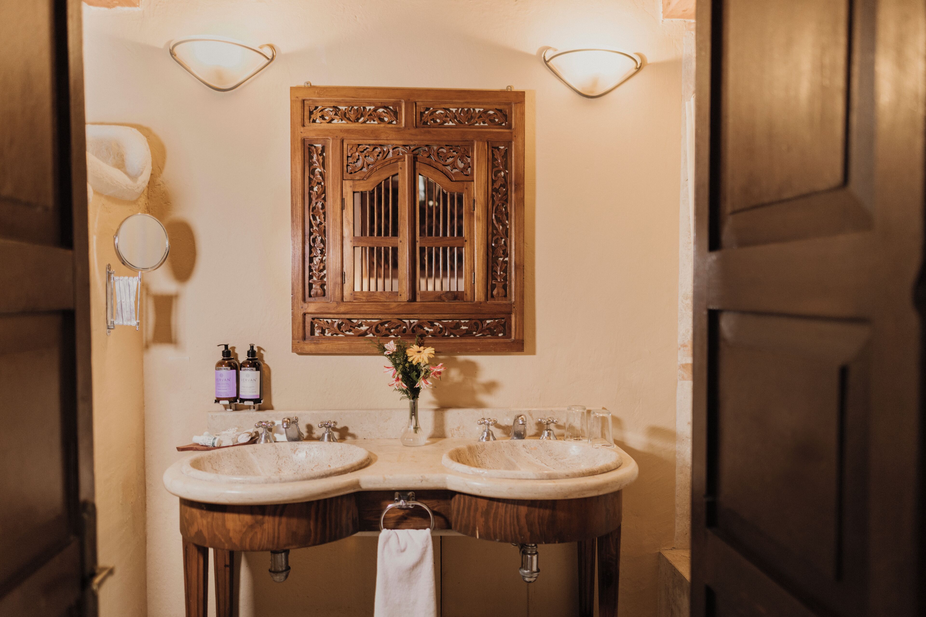 A bathroom with two sinks, a wooden vanity, a mirror with a decorative frame, and wall-mounted lights.