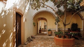 Une cour avec un sol en briques, des portes en arc de cercle et des plantes en pot.