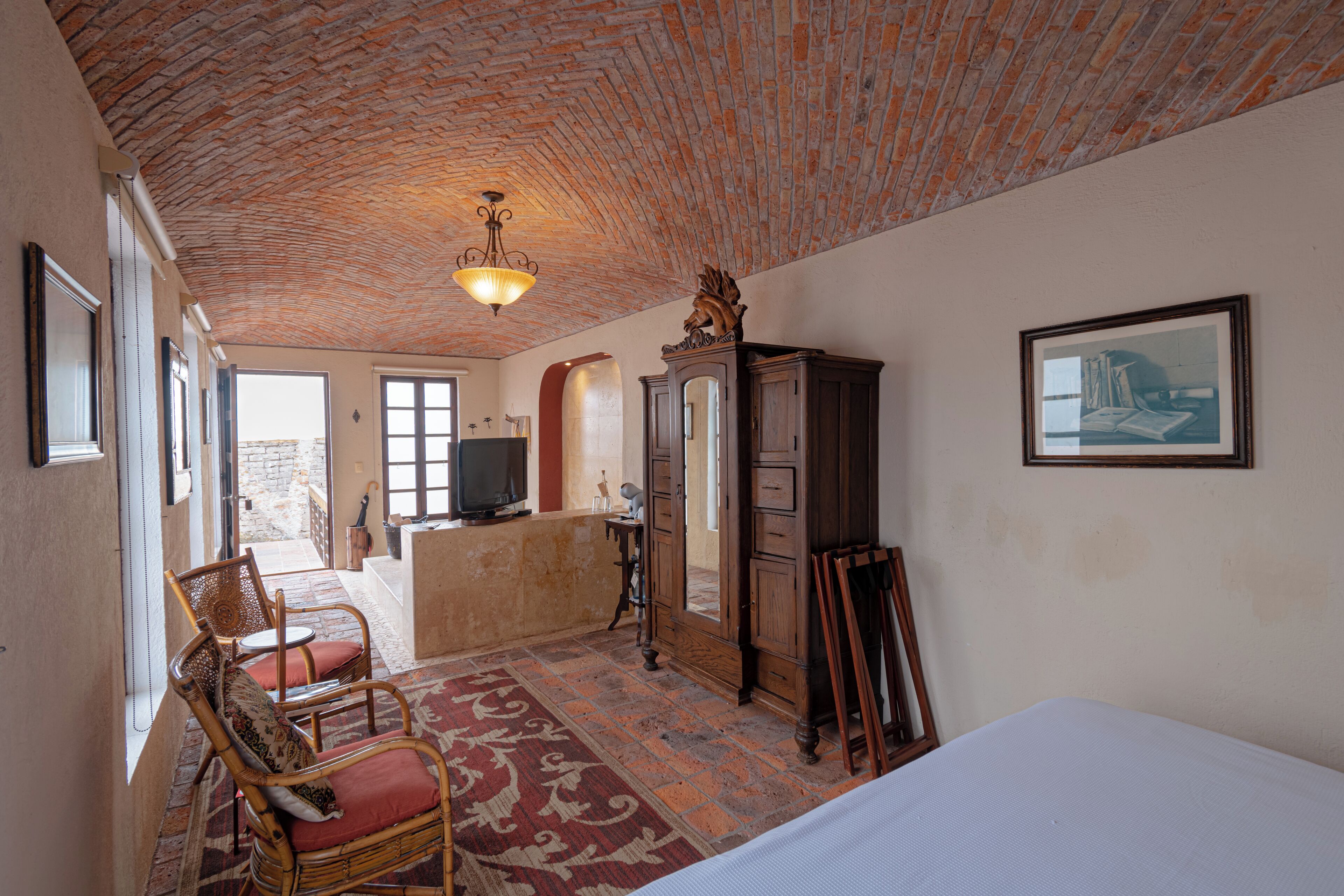 A room with a brick ceiling, a bed, a wooden cabinet, a chair, a desk, and a television.