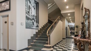 A grand staircase with a checkered floor, a large black and white mural, and a grand mirror. - Hotel Impero (Cremona)