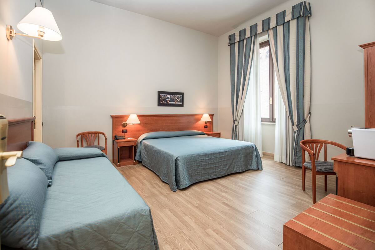 Habitación de hotel con dos camas, un escritorio, una computadora, una silla y una lámpara.