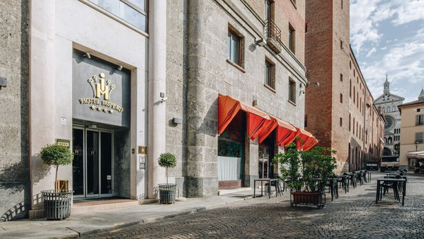 A historic building with a prominent hotel entrance, outdoor seating area, and cobblestone street. - Hotel Impero (Cremona)