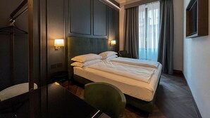 A hotel room with a bed, a desk, and a chair. There are two wall-mounted lamps and a window with curtains. - Hotel Impero (Cremona)