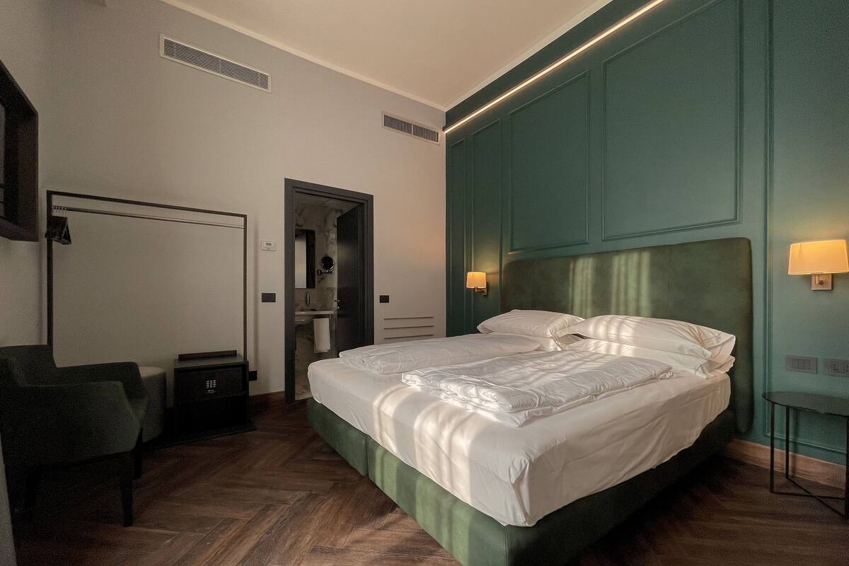 Habitación de hotel con una cama grande, un escritorio y una silla. Se ve un baño por una puerta abierta.
