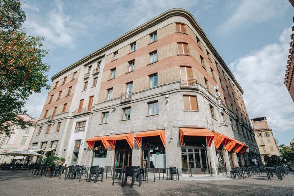 A historic building with a corner entrance, multiple balconies, and outdoor seating areas with orange awnings.