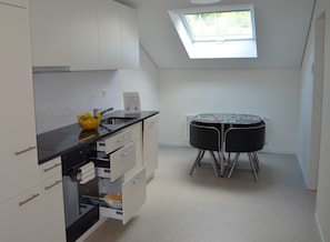 A compact kitchen with white cabinets, a black countertop, and a skylight. - Central Hotel Post (Chur)