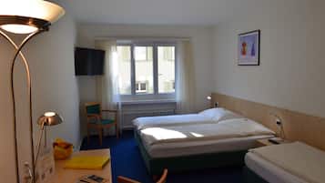 Habitación de hotel con dos camas, un escritorio, una silla, una lámpara, un televisor y una ventana con cortinas.
