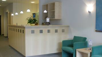 A reception area with a counter, a plant, and two green chairs.