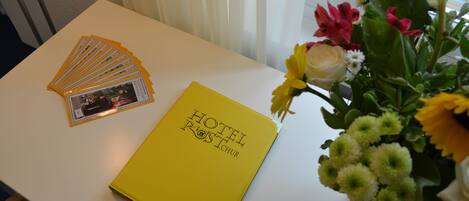 Un folleto amarillo con el título "HOTEL ROOSTICHUR" sobre una mesa blanca, junto a un ramo de flores.