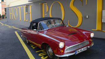 A red vintage car parked in front of a building with large yellow letters spelling "HOTEL POST".