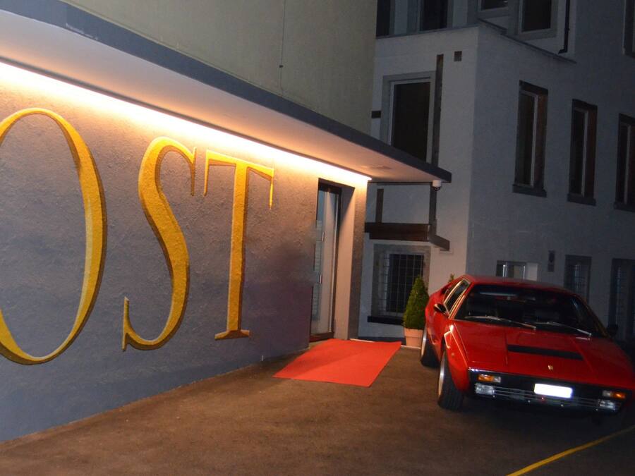 A building with a large illuminated sign reading "POST" and a red sports car parked in front.
