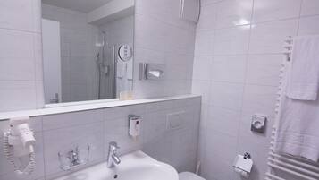 A modern bathroom with a white sink, mirror, and toilet. There is a hairdryer on the wall and a towel rack.