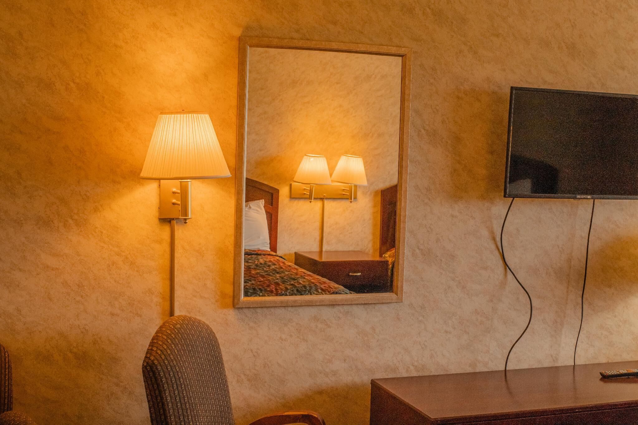 Une chambre d’hôtel dotée d’un grand miroir, d’un téléviseur à écran plat et d’une lampe.