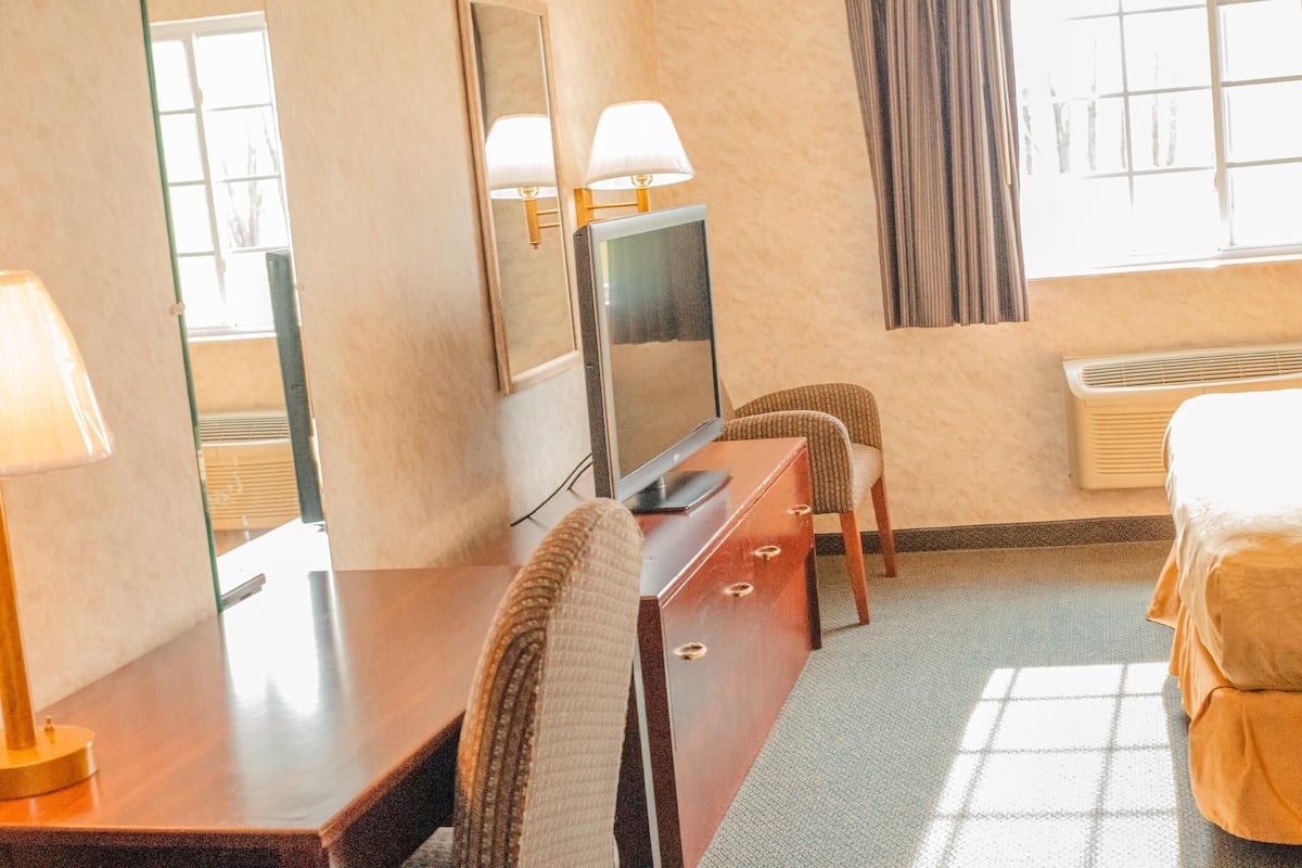 Una habitación de hotel con una cama, un escritorio con lámpara, un televisor y una silla.