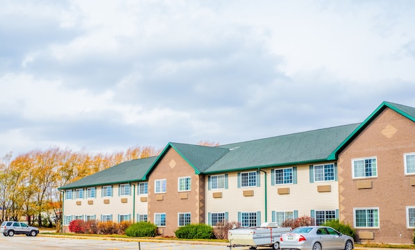 A multi-story hotel with a brick facade, multiple windows, and a parking lot with several cars.