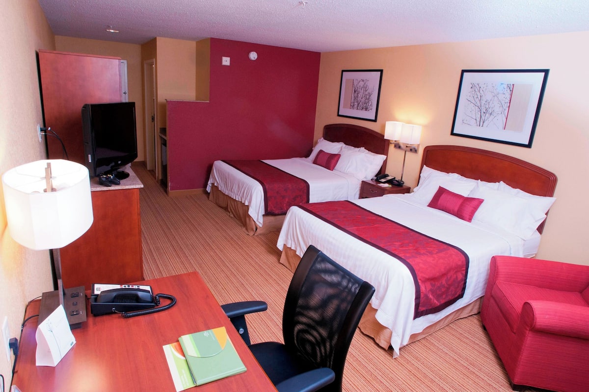 Ein Hotelzimmer mit zwei Betten, einem Schreibtisch mit Telefon, einem Sessel und einem Fernseher.