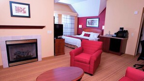Ein Hotelzimmer mit Kamin, einem Bett mit roter Bettwäsche, einem roten Sessel, einem Holztisch und einer Küchenzeile.