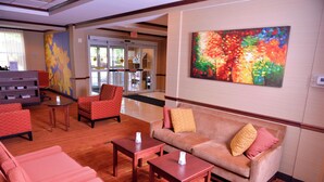 Eine Lobby mit einer Couch, Sesseln und einem Couchtisch. Ein Gemälde befindet sich an der Wand, und im Hintergrund ist eine Tür zu sehen.