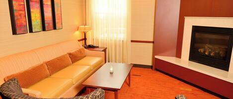 Habitación de hotel con sofá, sillones, una mesa de centro, chimenea y una pared decorada con arte abstracto.