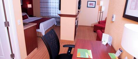 Una habitación de hotel con una cama, un escritorio con una silla, un sofá rojo y un televisor en la pared.