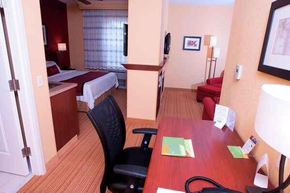 Una habitación de hotel con una cama, un escritorio con una silla, un sofá rojo y un televisor en la pared.