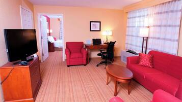 Une chambre d’hôtel avec une télévision, un canapé rouge, un fauteuil rouge, un bureau avec un ordinateur portable et un lit en arrière-plan.